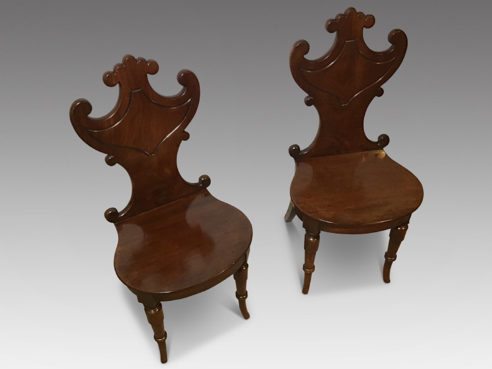 A pair of antique dark mahogany hall chairs featuring carved scroll backs, solid wood seats, and turned front legs. View III