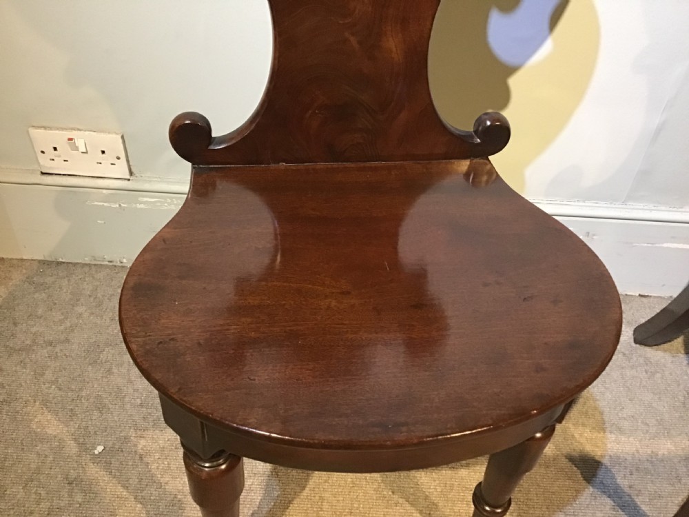 A pair of antique dark mahogany hall chairs featuring carved scroll backs, solid wood seats, and turned front legs. View IV