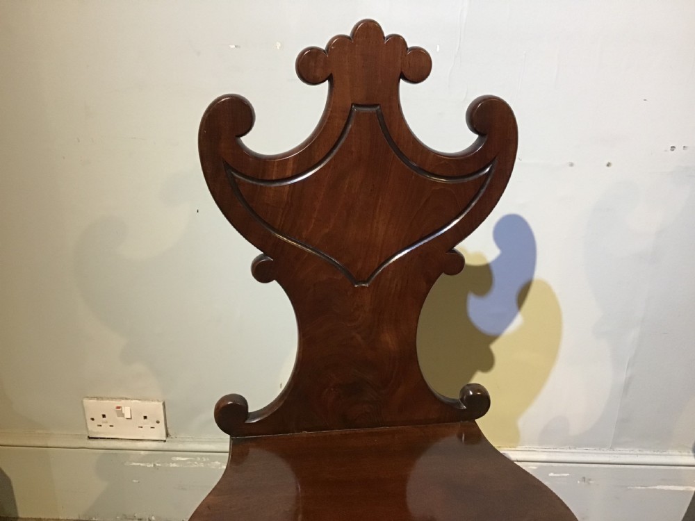A pair of antique dark mahogany hall chairs featuring carved scroll backs, solid wood seats, and turned front legs. View V
