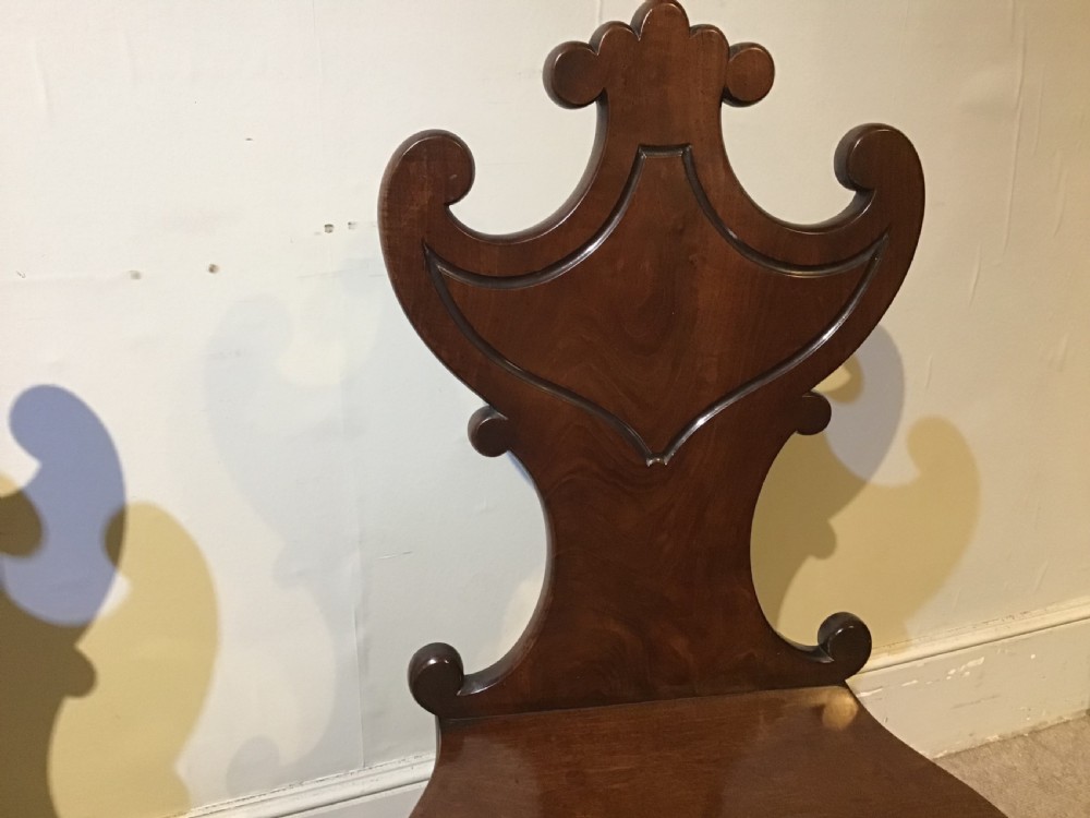 A pair of antique dark mahogany hall chairs featuring carved scroll backs, solid wood seats, and turned front legs. View VI