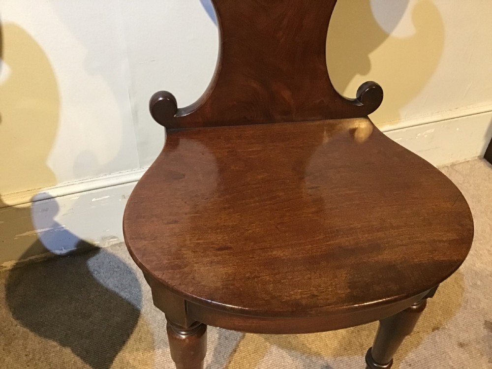 A pair of antique dark mahogany hall chairs featuring carved scroll backs, solid wood seats, and turned front legs. View VII