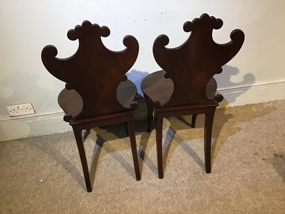 A pair of antique dark mahogany hall chairs featuring carved scroll backs, solid wood seats, and turned front legs. View XI