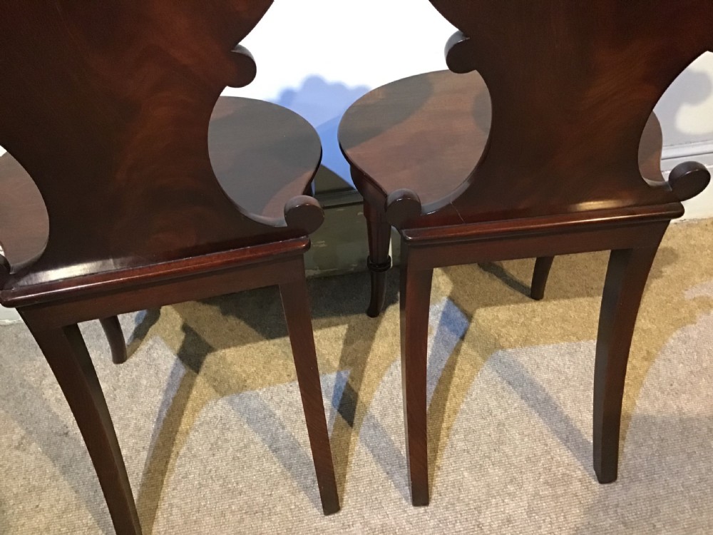 A pair of antique dark mahogany hall chairs featuring carved scroll backs, solid wood seats, and turned front legs. View XII