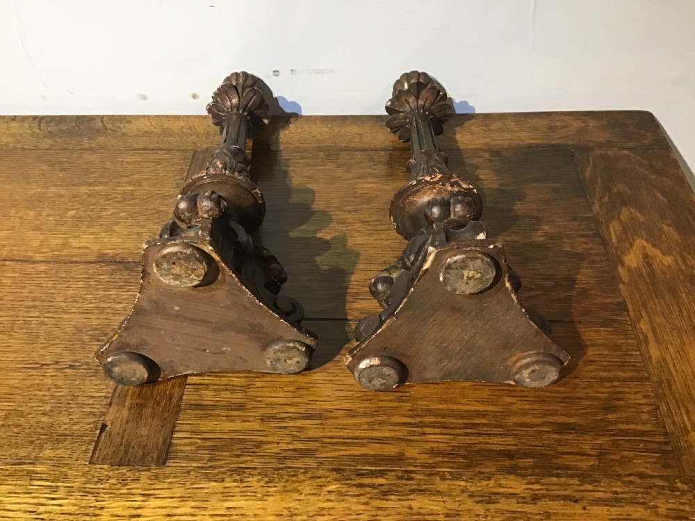 A pair of antique carved wood candlesticks featuring ornate scrolled tripod bases, fluted stems, and urn sconces with an aged dark patinated gilt finish. View II