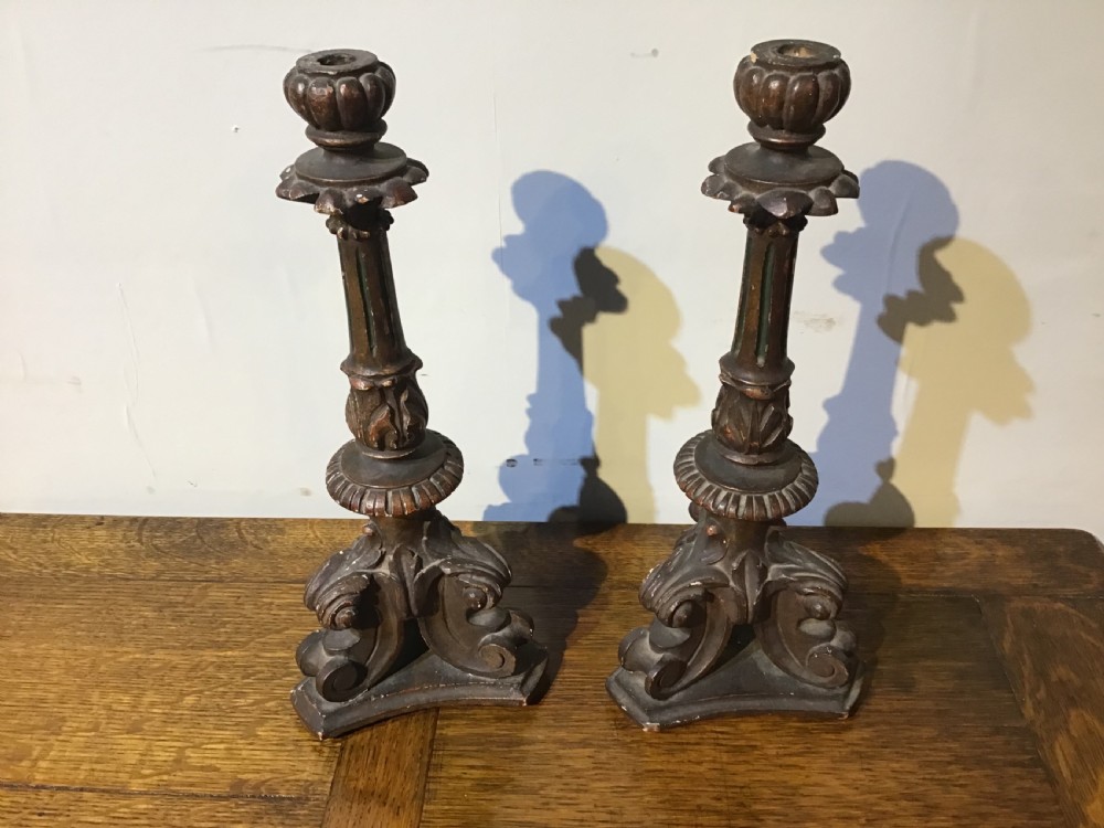 A pair of antique carved wood candlesticks featuring ornate scrolled tripod bases, fluted stems, and urn sconces with an aged dark patinated gilt finish. View III