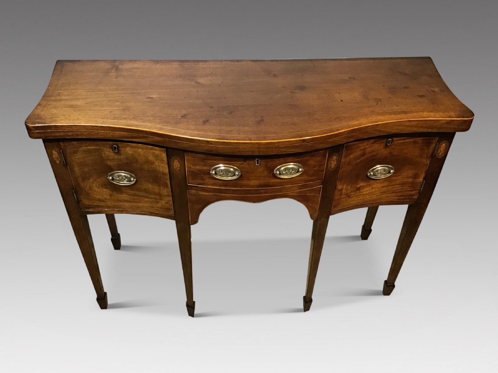A Georgian style mahogany sideboard featuring a serpentine front, inlaid oval motifs on tapered legs, and brass handles.