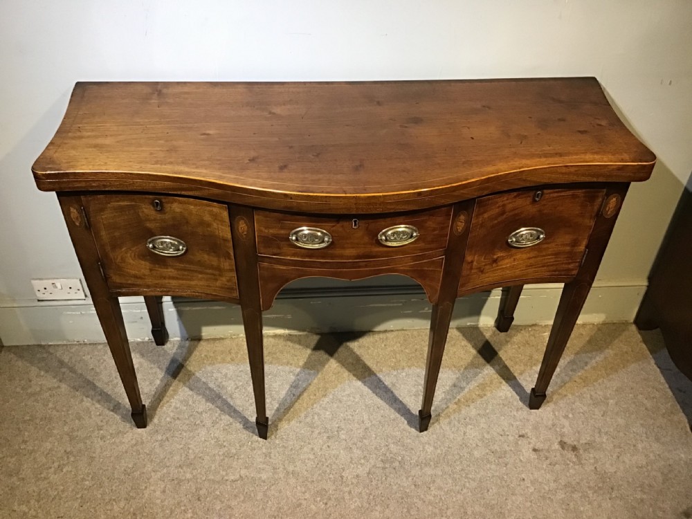 A Georgian style mahogany sideboard featuring a serpentine front, inlaid oval motifs on tapered legs, and brass handles. View II