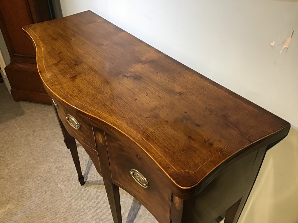 A Georgian style mahogany sideboard featuring a serpentine front, inlaid oval motifs on tapered legs, and brass handles. View III