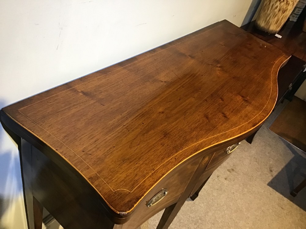 A Georgian style mahogany sideboard featuring a serpentine front, inlaid oval motifs on tapered legs, and brass handles. View V