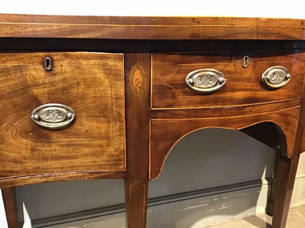 A Georgian style mahogany sideboard featuring a serpentine front, inlaid oval motifs on tapered legs, and brass handles. View VI