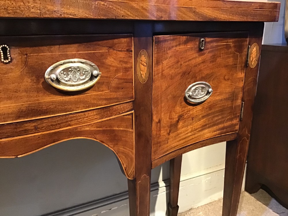 A Georgian style mahogany sideboard featuring a serpentine front, inlaid oval motifs on tapered legs, and brass handles. View VIII