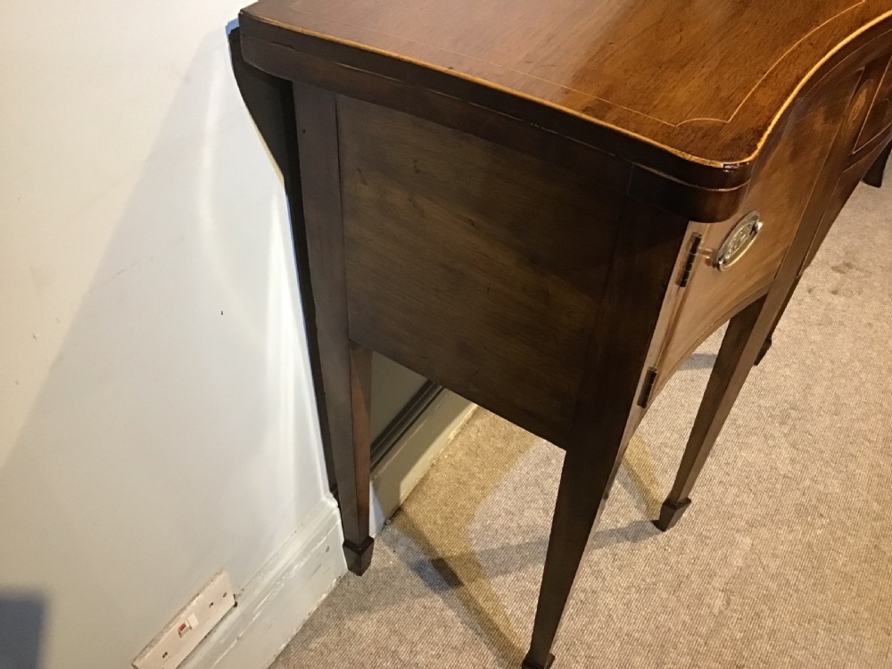 A Georgian style mahogany sideboard featuring a serpentine front, inlaid oval motifs on tapered legs, and brass handles. View X