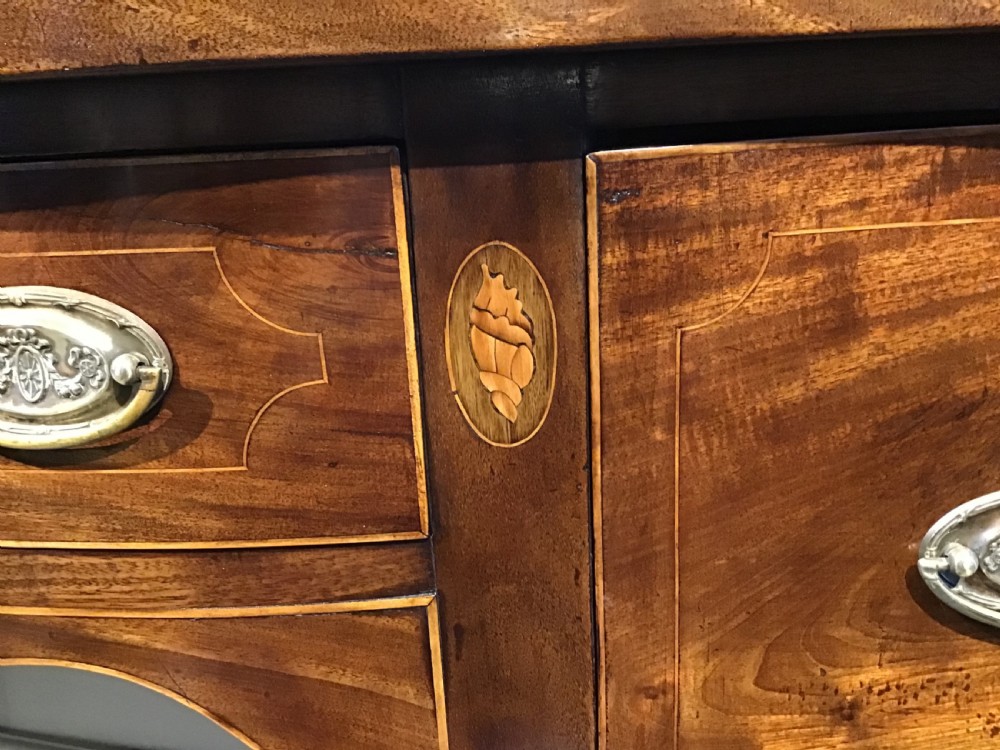 A Georgian style mahogany sideboard featuring a serpentine front, inlaid oval motifs on tapered legs, and brass handles. View XIII