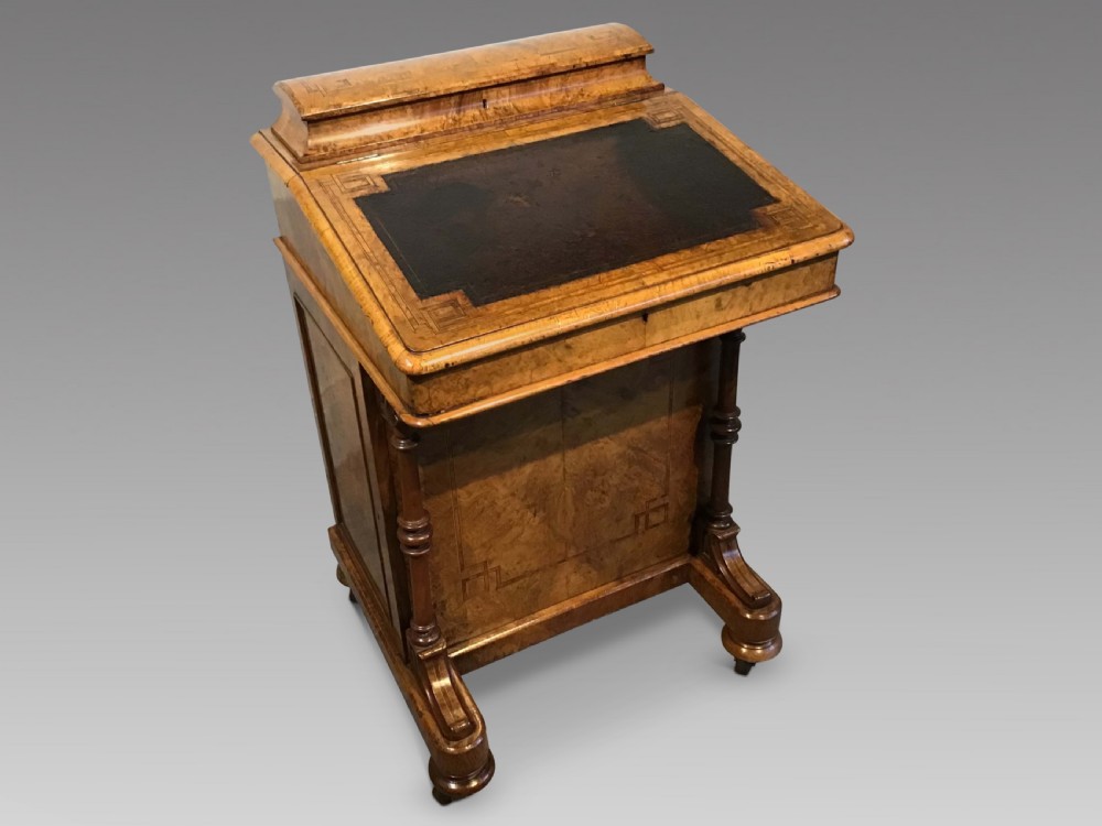A Victorian burr walnut Davenport desk featuring a sloped leather writing surface, inlaid wood corner detailing, turned front supports, and a top stationery compartment.
