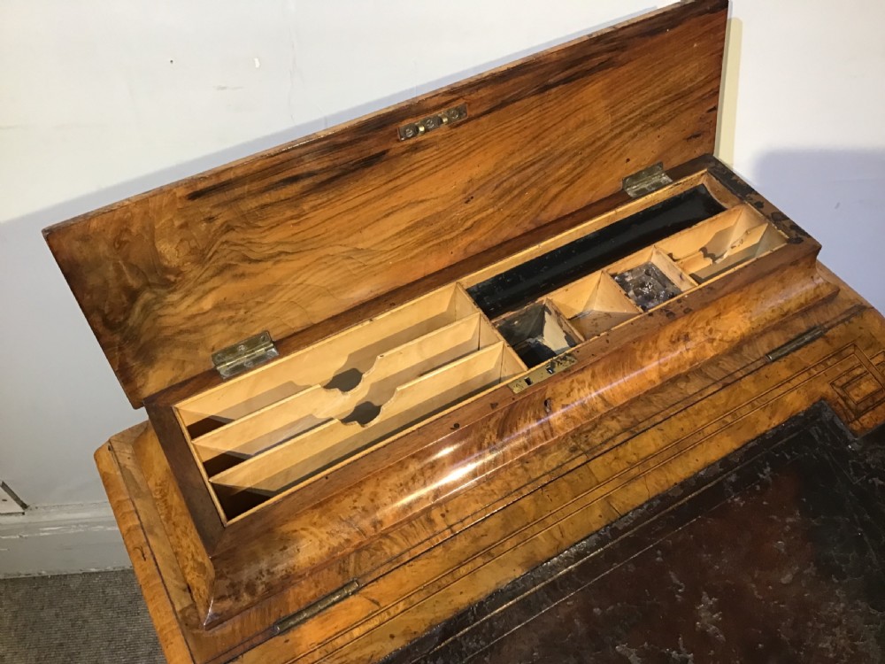 A Victorian burr walnut Davenport desk featuring a sloped leather writing surface, inlaid wood corner detailing, turned front supports, and a top stationery compartment. View VI