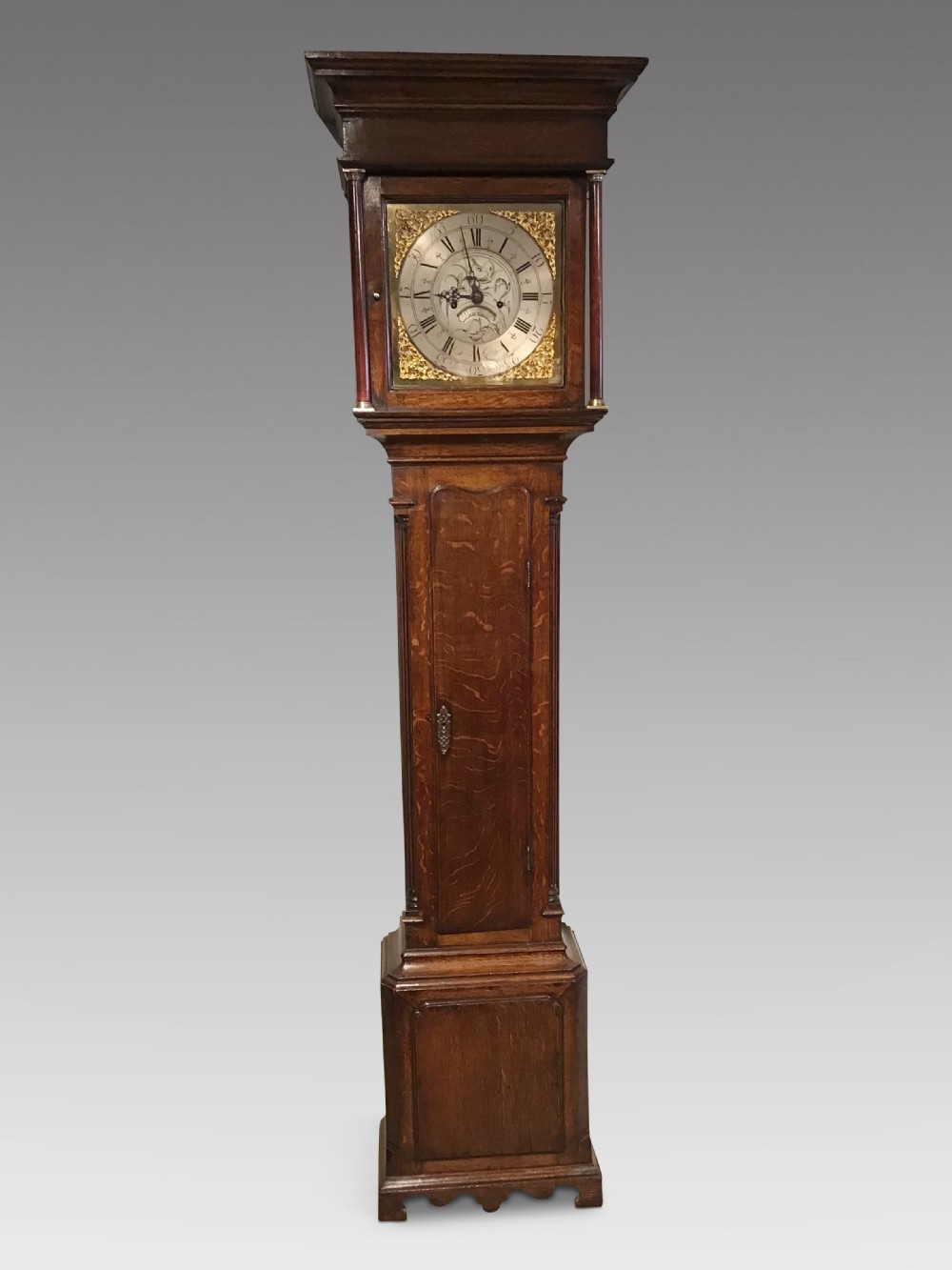 A Georgian oak eight-day longcase clock featuring an engraved brass dial, fluted hood columns, and a tall timber trunk resting on bracket feet.