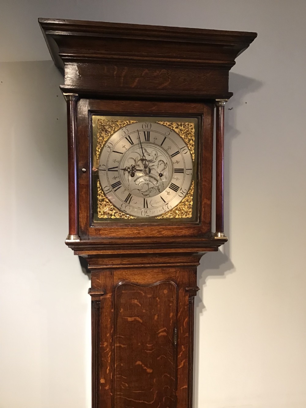 A Georgian oak eight-day longcase clock featuring an engraved brass dial, fluted hood columns, and a tall timber trunk resting on bracket feet. View II