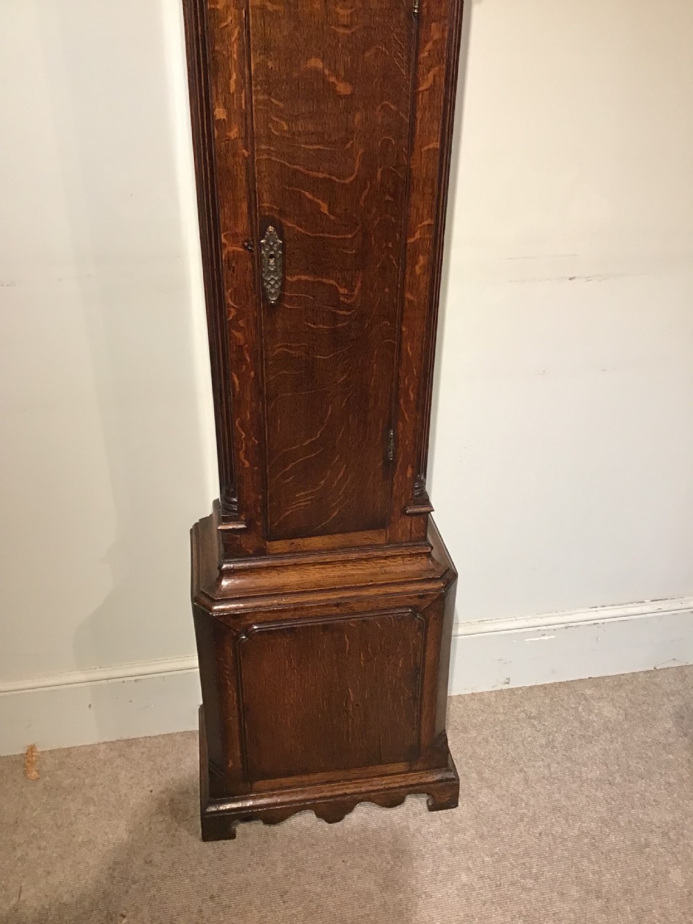 A Georgian oak eight-day longcase clock featuring an engraved brass dial, fluted hood columns, and a tall timber trunk resting on bracket feet. View V