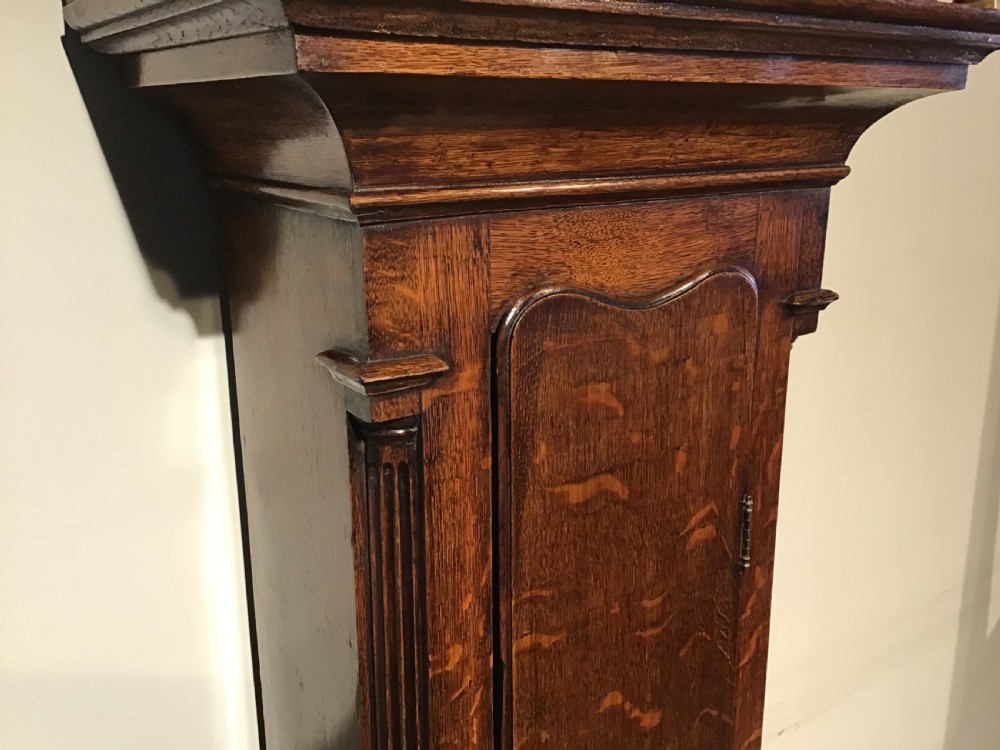 A Georgian oak eight-day longcase clock featuring an engraved brass dial, fluted hood columns, and a tall timber trunk resting on bracket feet. View VIII