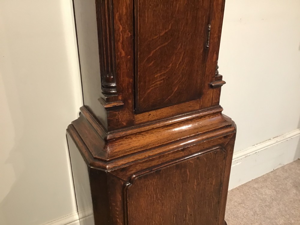 A Georgian oak eight-day longcase clock featuring an engraved brass dial, fluted hood columns, and a tall timber trunk resting on bracket feet. View IX