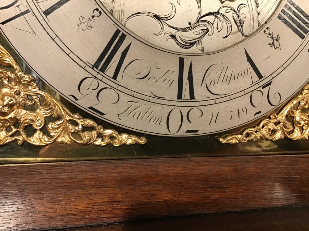 A Georgian oak eight-day longcase clock featuring an engraved brass dial, fluted hood columns, and a tall timber trunk resting on bracket feet. View XII