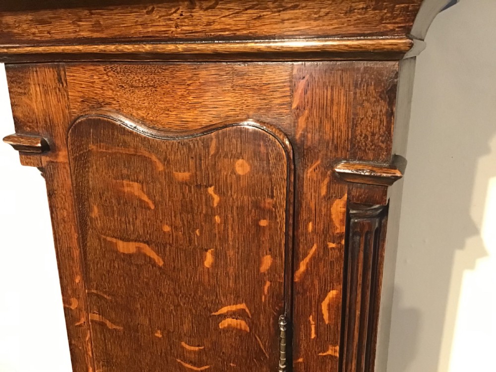 A Georgian oak eight-day longcase clock featuring an engraved brass dial, fluted hood columns, and a tall timber trunk resting on bracket feet. View XIII