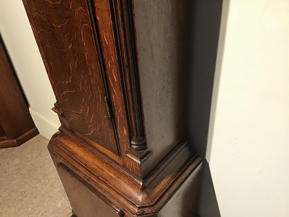 A Georgian oak eight-day longcase clock featuring an engraved brass dial, fluted hood columns, and a tall timber trunk resting on bracket feet. View XIV