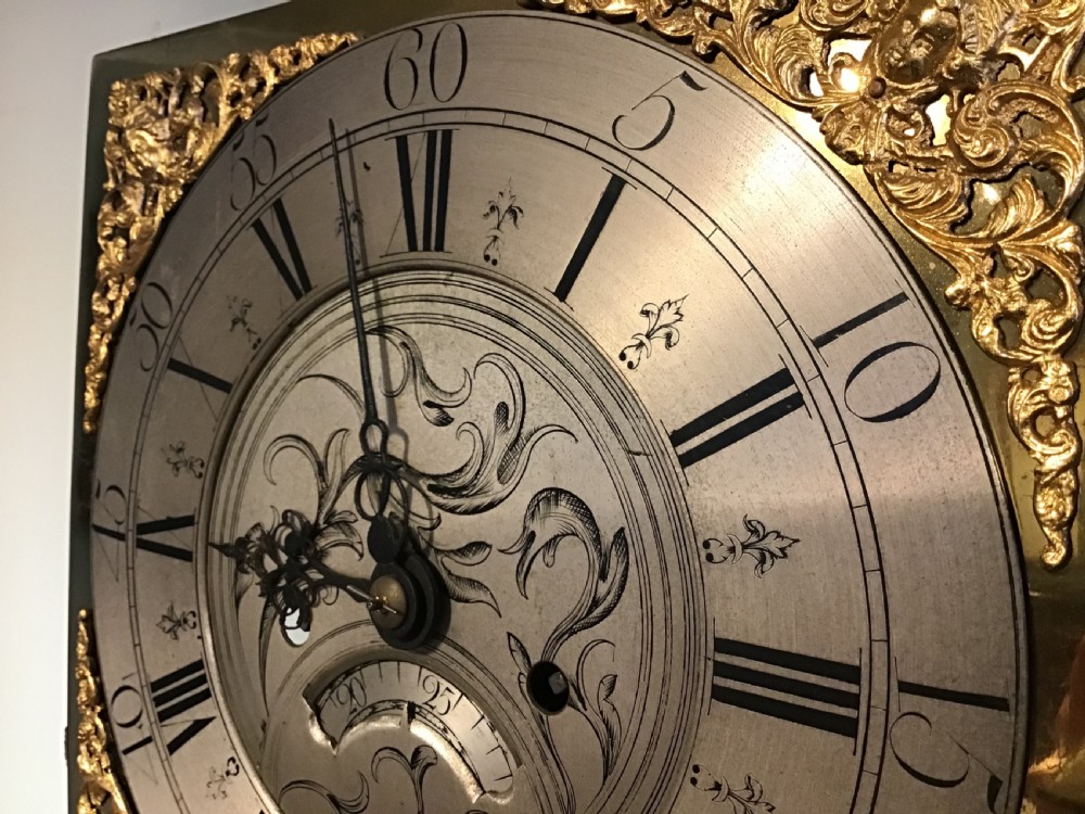 A Georgian oak eight-day longcase clock featuring an engraved brass dial, fluted hood columns, and a tall timber trunk resting on bracket feet. View XV