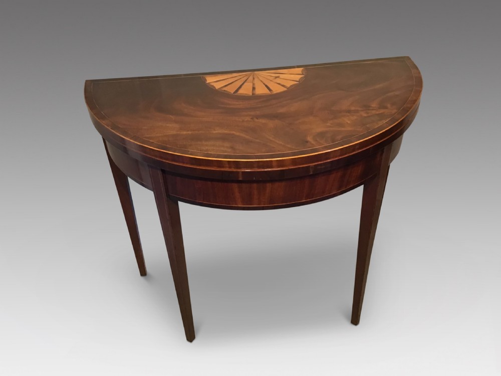 A Georgian dark mahogany demi-lune console table featuring a semicircular top with a central fan inlay motif and square tapered legs.