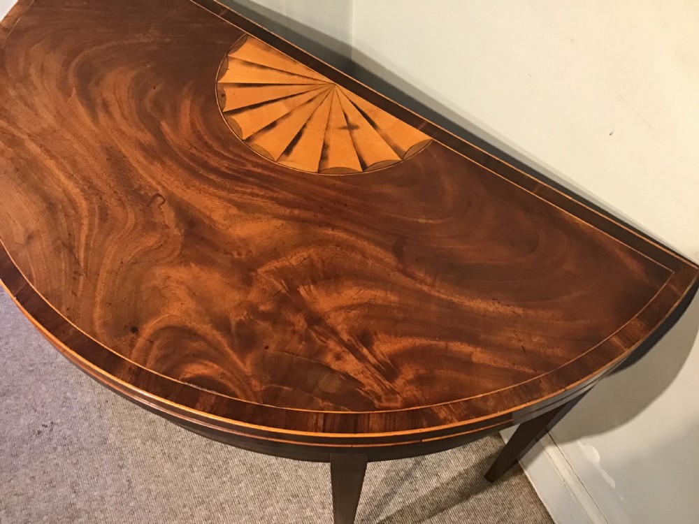 A Georgian dark mahogany demi-lune console table featuring a semicircular top with a central fan inlay motif and square tapered legs. View V