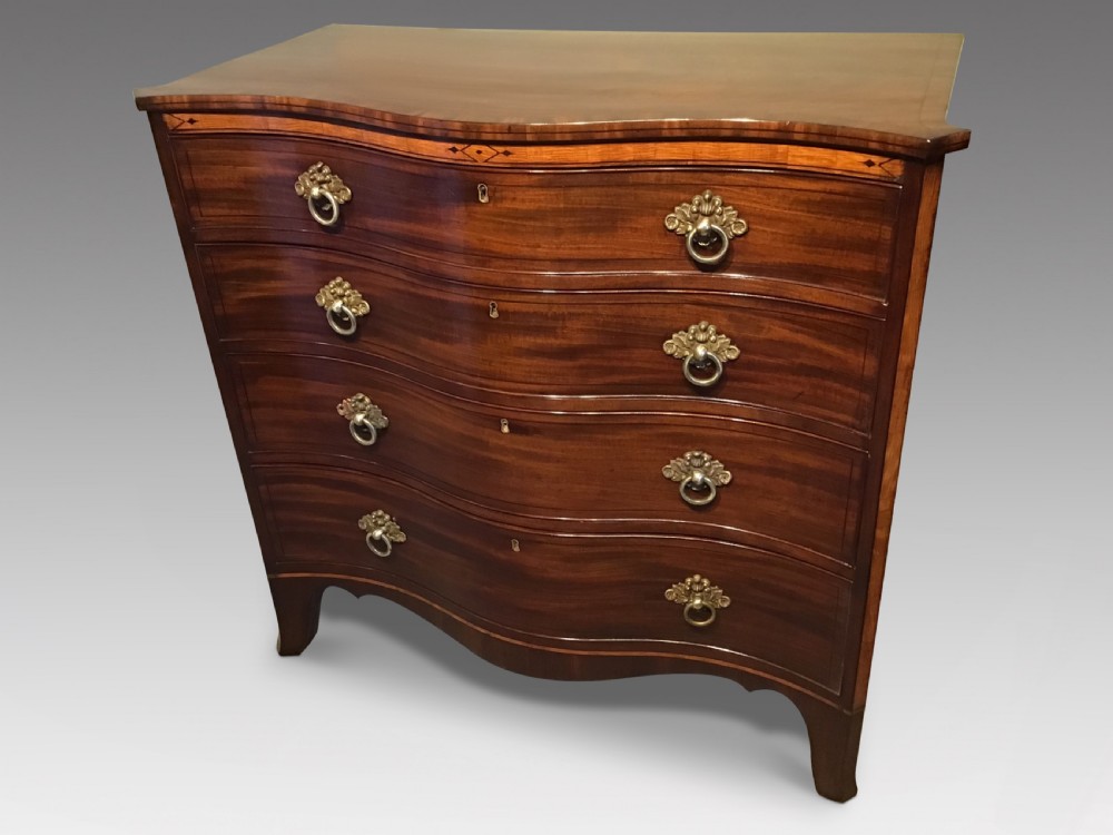 A George III style flame mahogany serpentine chest of drawers featuring four graduated drawers with brass ring handles and splayed feet.