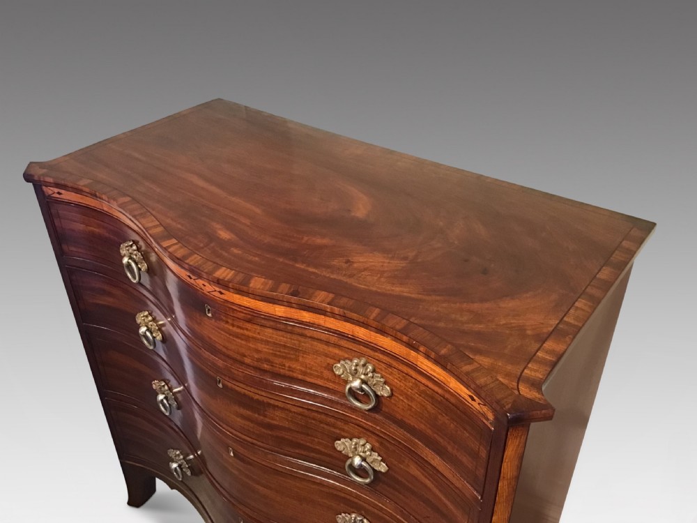 A George III style flame mahogany serpentine chest of drawers featuring four graduated drawers with brass ring handles and splayed feet. View II