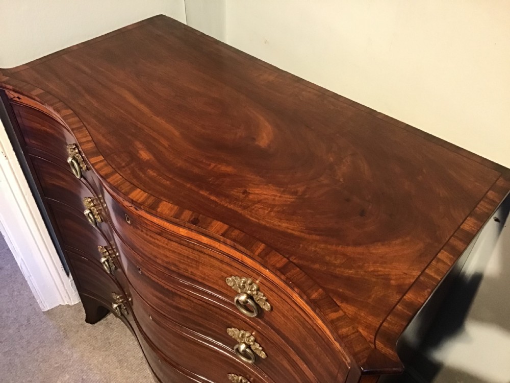 A George III style flame mahogany serpentine chest of drawers featuring four graduated drawers with brass ring handles and splayed feet. View III