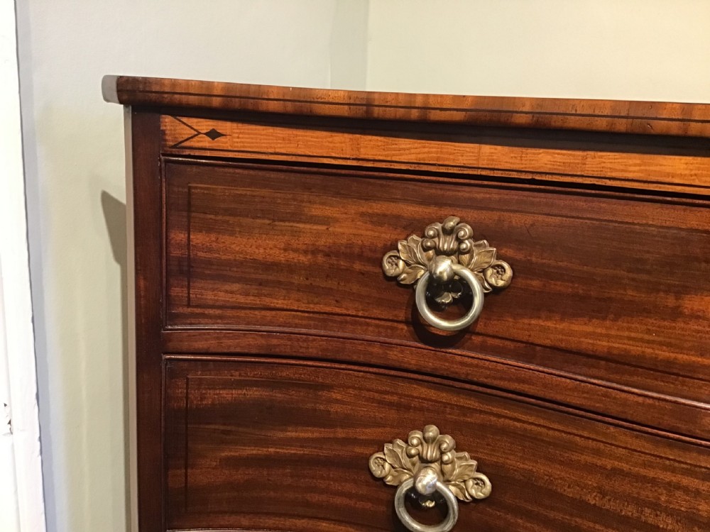 A George III style flame mahogany serpentine chest of drawers featuring four graduated drawers with brass ring handles and splayed feet. View V