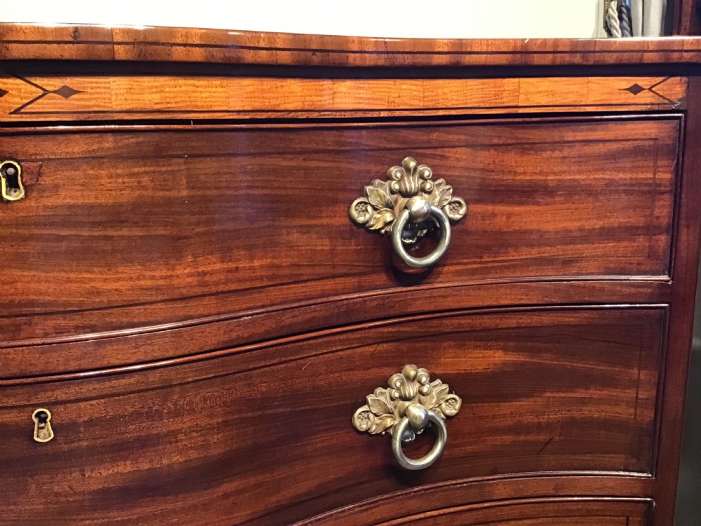 A George III style flame mahogany serpentine chest of drawers featuring four graduated drawers with brass ring handles and splayed feet. View VI