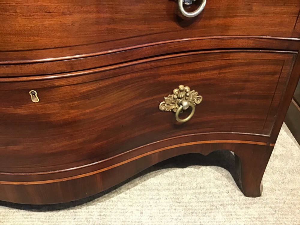 A George III style flame mahogany serpentine chest of drawers featuring four graduated drawers with brass ring handles and splayed feet. View VII