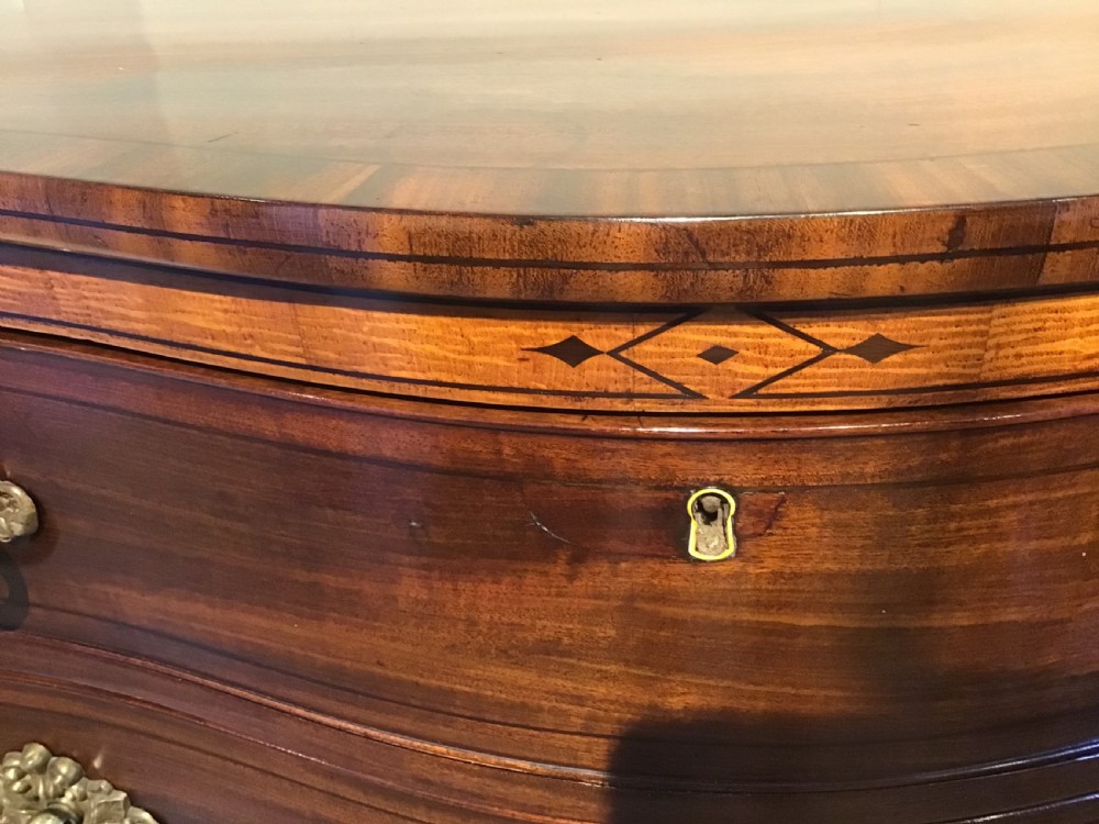 A George III style flame mahogany serpentine chest of drawers featuring four graduated drawers with brass ring handles and splayed feet. View IX