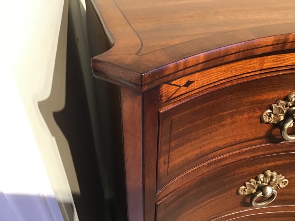A George III style flame mahogany serpentine chest of drawers featuring four graduated drawers with brass ring handles and splayed feet. View X