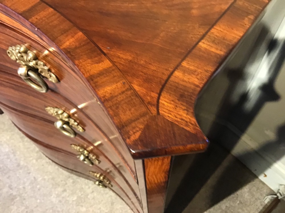 A George III style flame mahogany serpentine chest of drawers featuring four graduated drawers with brass ring handles and splayed feet. View XI