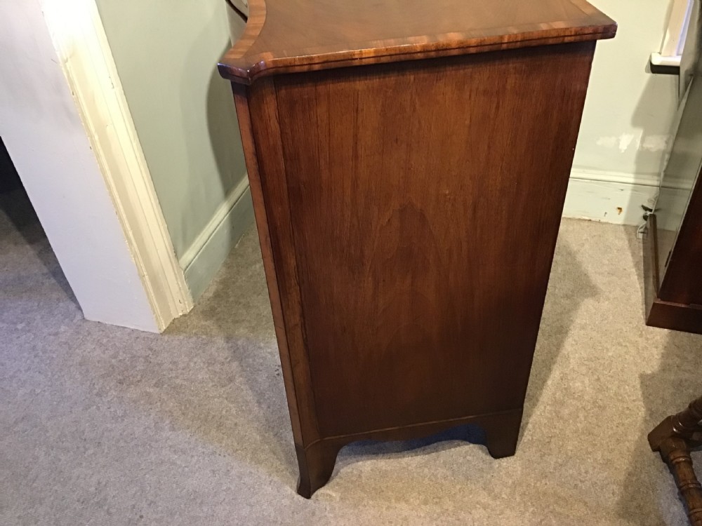 A George III style flame mahogany serpentine chest of drawers featuring four graduated drawers with brass ring handles and splayed feet. View XII