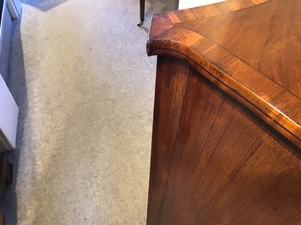 A George III style flame mahogany serpentine chest of drawers featuring four graduated drawers with brass ring handles and splayed feet. View XIII