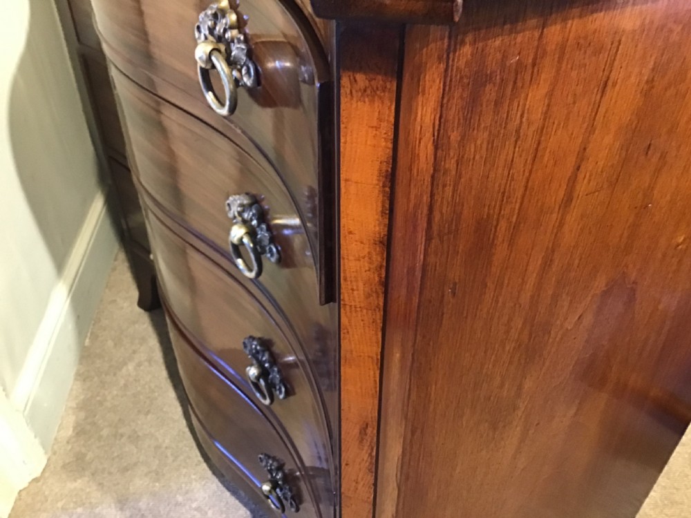 A George III style flame mahogany serpentine chest of drawers featuring four graduated drawers with brass ring handles and splayed feet. View XIV