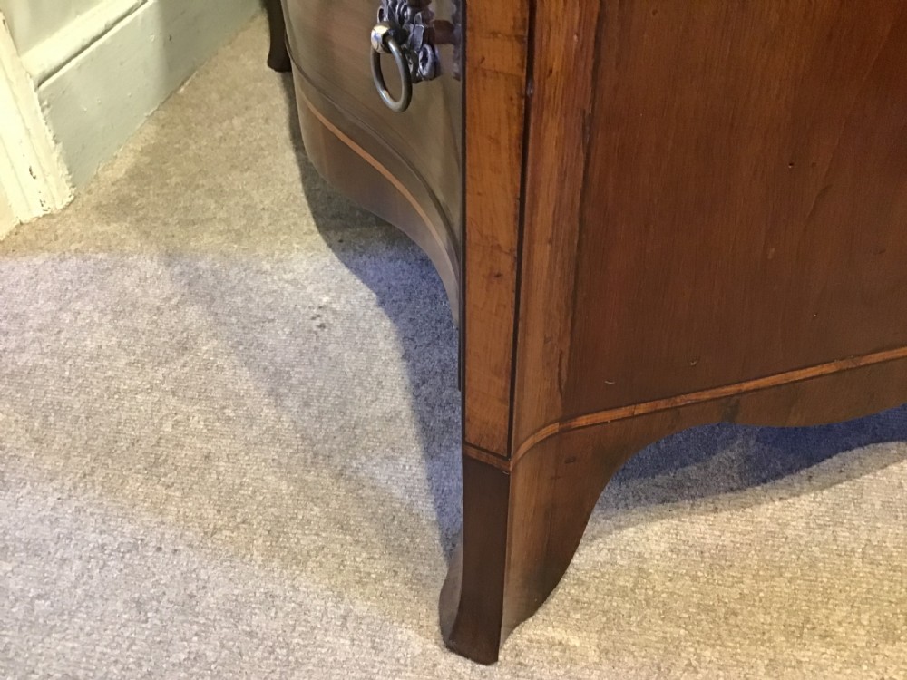 A George III style flame mahogany serpentine chest of drawers featuring four graduated drawers with brass ring handles and splayed feet. View XV