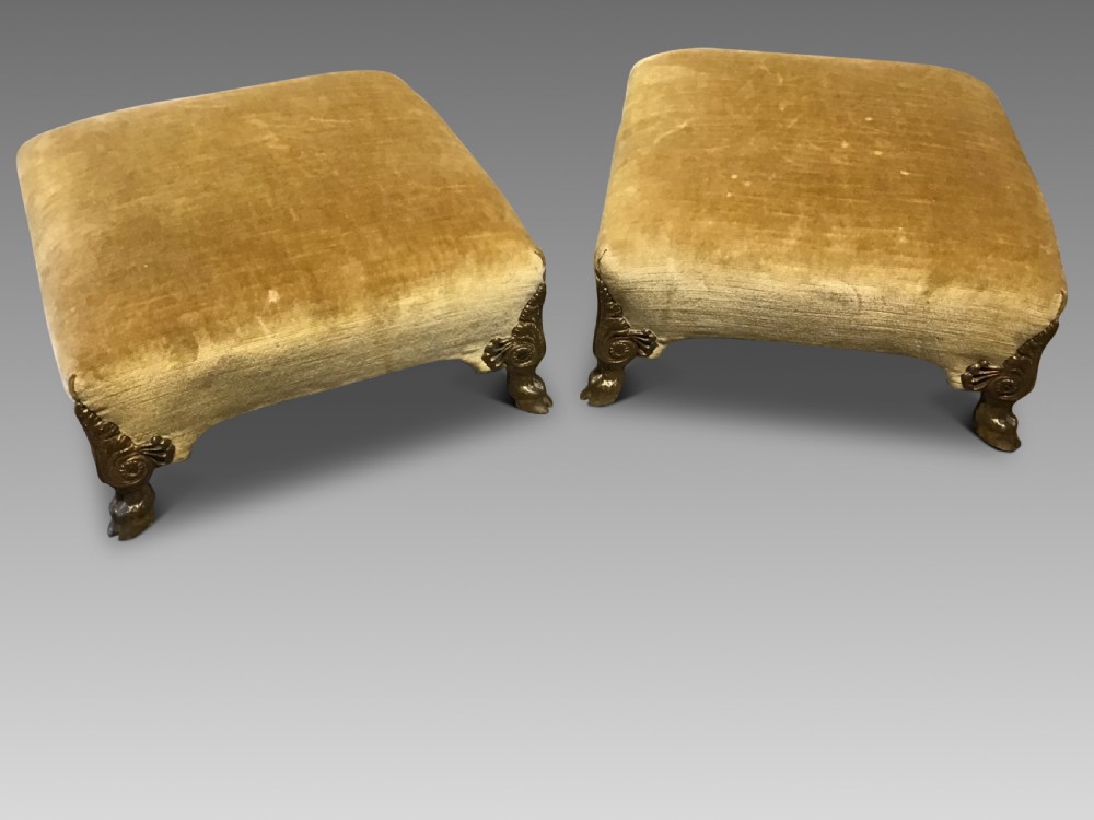 A pair of low rectangular antique footstools upholstered in mustard gold velvet with ornate carved cabriole legs.