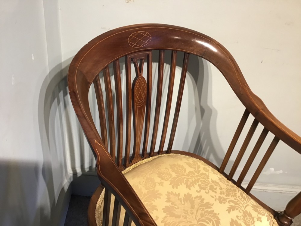 An Edwardian mahogany tub armchair featuring inlaid wood decoration, slender spindles, and a light yellow upholstered seat. View II