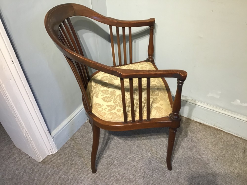 An Edwardian mahogany tub armchair featuring inlaid wood decoration, slender spindles, and a light yellow upholstered seat. View V