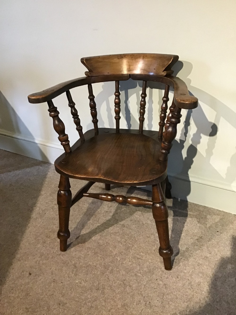 A Victorian smokers bow armchair crafted from polished dark timber, featuring turned spindles, a horseshoe armrest, and a contoured seat.