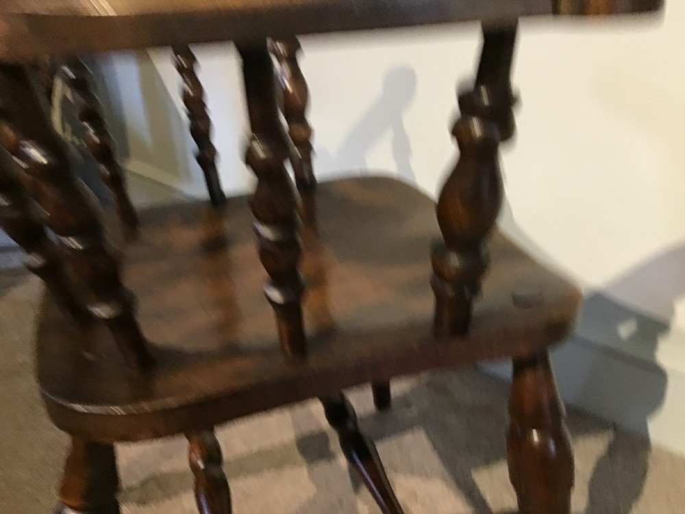 A Victorian smokers bow armchair crafted from polished dark timber, featuring turned spindles, a horseshoe armrest, and a contoured seat. View X