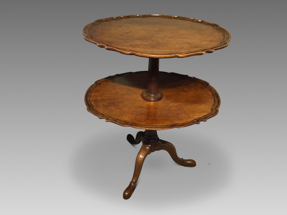 An antique mahogany two-tiered dumb waiter featuring scalloped tray edges, a turned central column, and a tripod base.