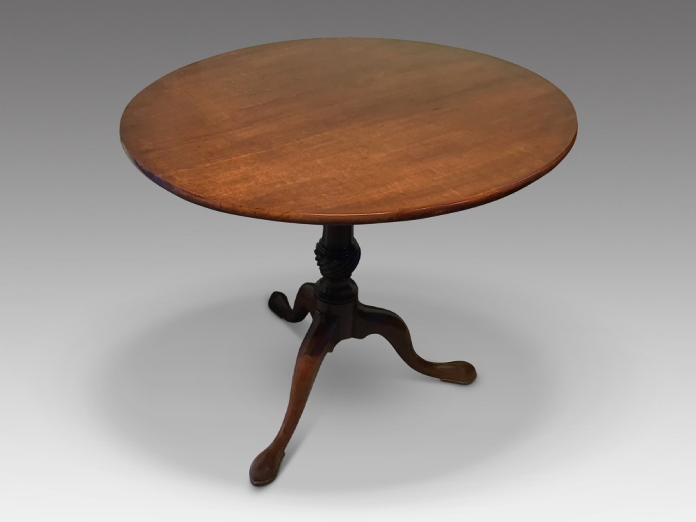 A dark mahogany circular tripod table with a turned central column featuring spiral carving and three cabriole legs with pad feet.